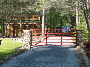 Traditional lodge nestled in a forested area, surrounded by a stone wall and a well-maintained gravel path.