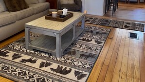 Ein gemütliches Wohnzimmer mit Holzboden, einer Couch, einem Couchtisch und einer Essecke mit Stühlen und einem Tisch.