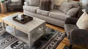 Ein Wohnzimmer mit einer holzverkleideten Wand, einem grauen Sofa, einem grauen Sessel, einem Couchtisch und gemusterten Teppichen.