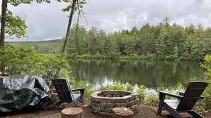 Ein Sitzbereich am Seeufer mit Adirondack-Stühlen und einer Steinkaminanlage.