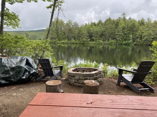 A lakeside seating area with Adirondack chairs and a stone fire pit.