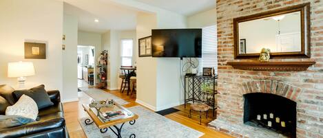 A living room with a fireplace, a television mounted on the wall, and a dining area in the background.