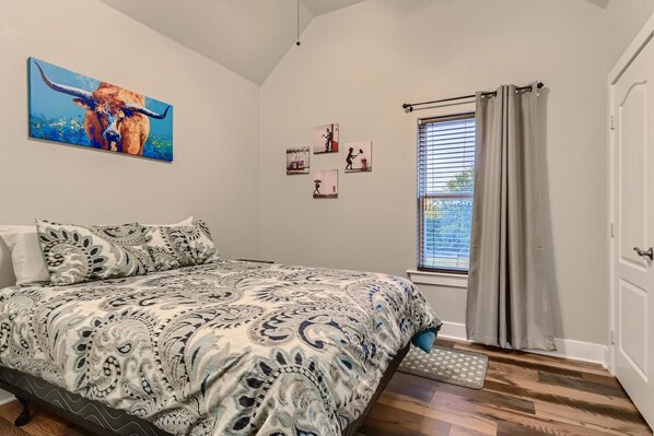 A bedroom with a bed, a painting of a bull, and a window with curtains.