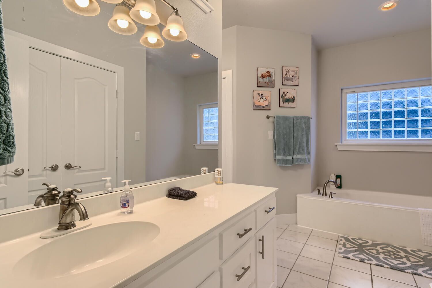 A modern bathroom with a large mirror, a white sink, a bathtub, and a window with frosted glass.