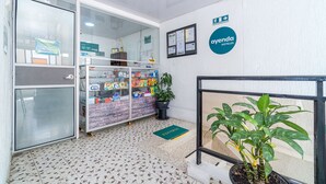 Un área de recepción con puerta de vidrio, un tablón de anuncios, una planta en maceta y un letrero que dice 'ayenda hotels'.