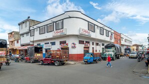 Un hotel de fachada blanca, con varios letreros, vista a la calle con vehículos estacionados y peatones.
