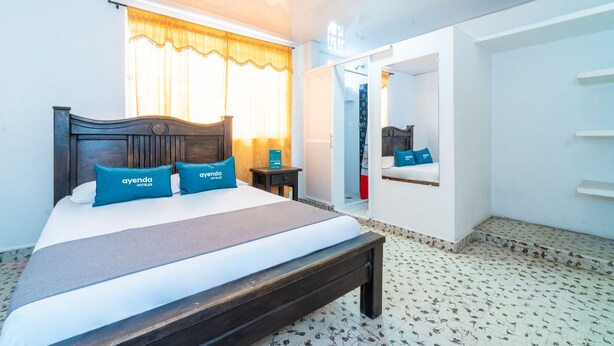 Habitación de hotel con cama, banca, armario y espejo.