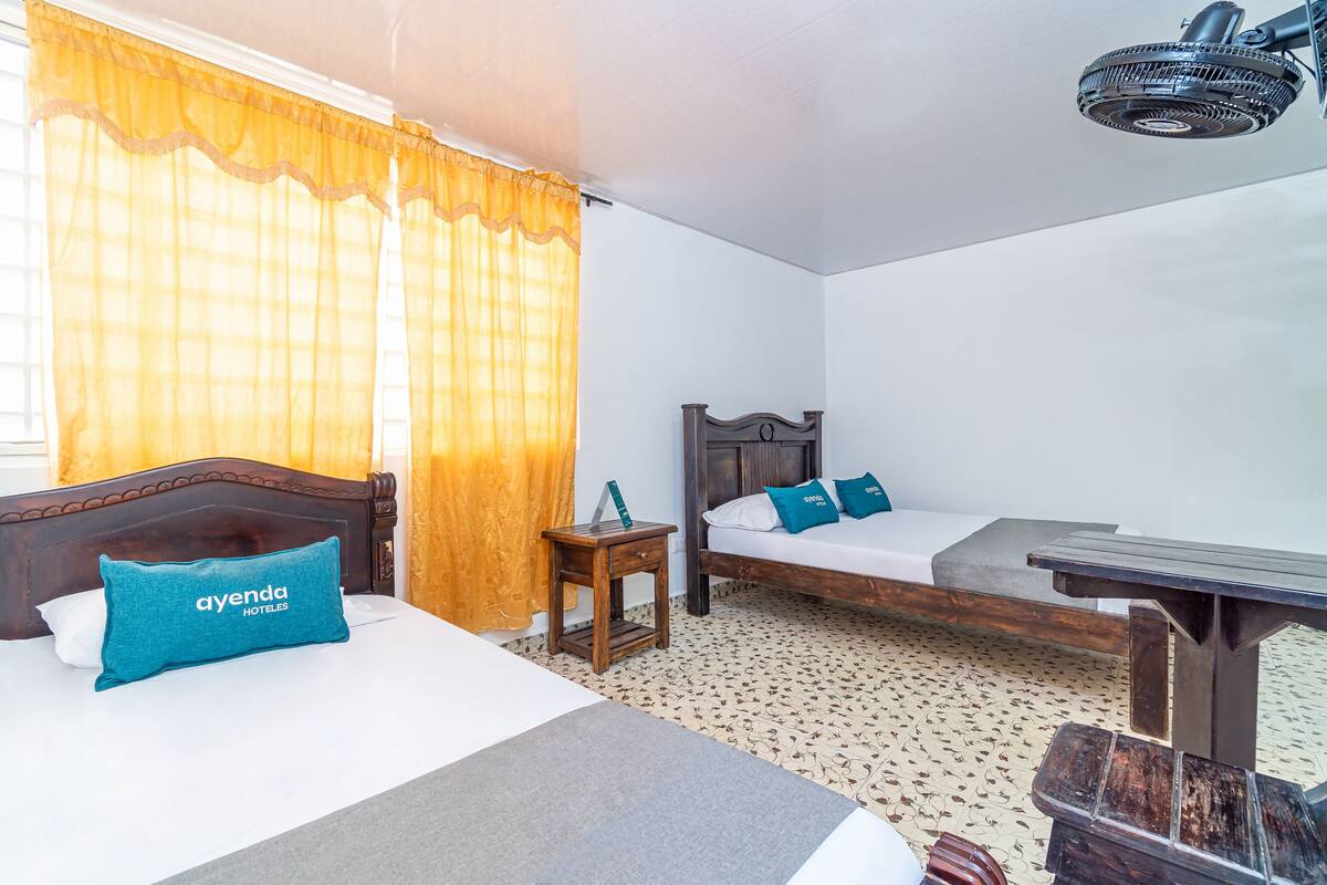 Een hotelkamer met twee bedden, een houten nachtkastje, een tafel en een plafondventilator.