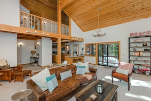 A spacious living area with a high ceiling and wooden beams, a brown leather sofa, a coffee table, and a bookshelf.