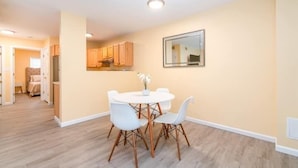 Un espace repas avec une table et des chaises blanches, des murs de couleur beige et un plancher en bois.