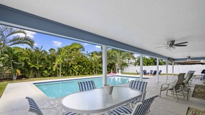 Ein überdachter Außenbereich mit Pool, Liegestühlen und einem Tisch.