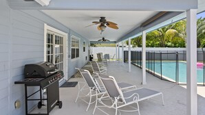 Eine überdachte Terrasse mit Grill, Liegestühlen und Pool.