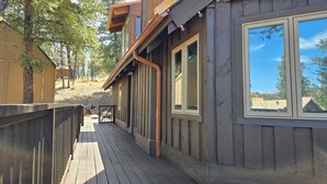 Eine Holzterrasse führt zu einer Hütte mit großen Fenstern und Blick auf den umliegenden Wald.