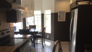 A kitchen with a stainless steel sink, a dining table with chairs, and a refrigerator.