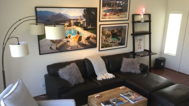 A living room with a black leather sofa, a white armchair, a wooden coffee table with books, and a floor lamp.