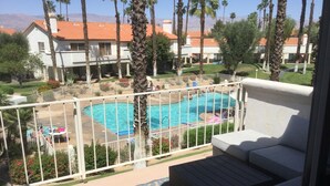 A pool area with a white fence, lounge chairs, and a view of a residential neighborhood with palm trees and houses.