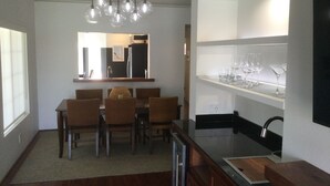 A modern kitchen with a dining area, featuring a wooden table, chairs, and a hanging light fixture.