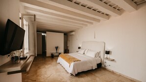 Une chambre avec un grand lit, un téléviseur posé sur un meuble, et un couloir menant à une autre pièce.