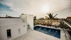 Une piscine sur le toit offrant une vue dégagée sur les gratte-ciel de la ville, un bâtiment blanc aux petites fenêtres et un palmier.