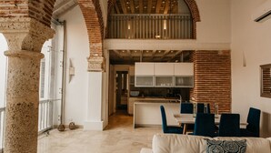 Un vaste espace de vie doté d’un haut plafond, d’arcs en briques apparentes, d’une cuisine moderne et d’un coin salon confortable avec un canapé blanc et des fauteuils bleus.