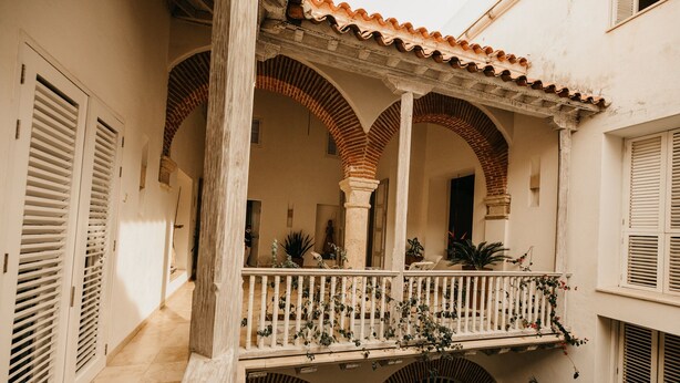 Une cour dotée d’un balcon couvert, d’arcades et de plantes en pot.