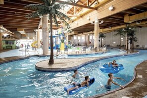 Piscina interior com teto de madeira, palmeiras e espreguiçadeiras.