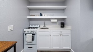 Une cuisine de taille réduite avec des meubles blancs, une cuisinière, un évier et une machine à café.