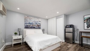 Une chambre à coucher moderne avec un grand lit, une petite table de chevet avec une lampe, un réfrigérateur et un tableau accroché au mur.
