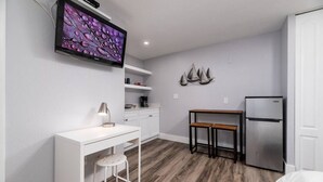 A compact kitchen with a white countertop, a small wooden table, a white chair, a built-in oven, and a refrigerator. - Shell on the Beach #104 (Hollywood)