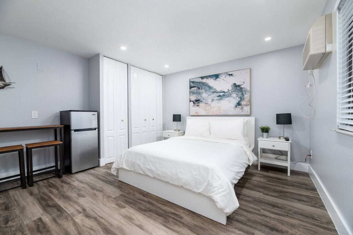 Une chambre à coucher comprenant un lit, un bureau, un réfrigérateur, une table de chevet et un climatiseur fixé au mur.