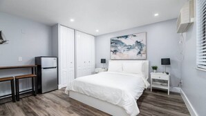 A bedroom with a bed, a desk, a refrigerator, a nightstand, and a wall-mounted air conditioner. - Shell on the Beach #104 (Hollywood)