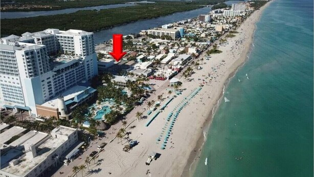 An aerial view of a coastal hotel area with multiple buildings, a beach, and a marina. - Shell on the Beach #104 (Hollywood)