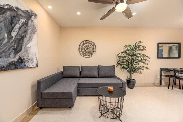 A modern living room with a grey sectional sofa, a round metal table, a potted plant, and artwork on the walls.