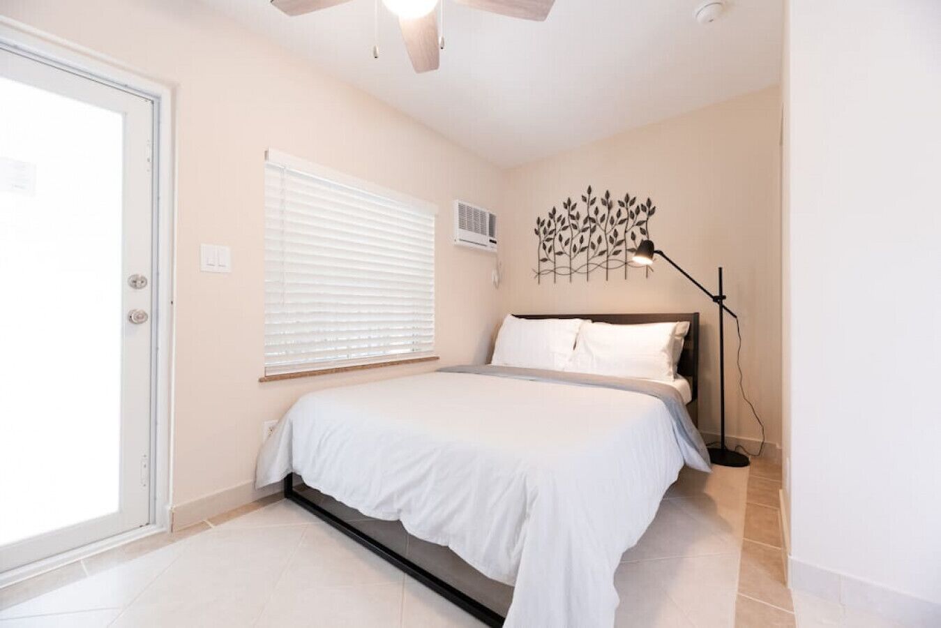 Quarto com cama, ventoinha no teto, janela com persianas, ar-condicionado fixado na parede e abajur.