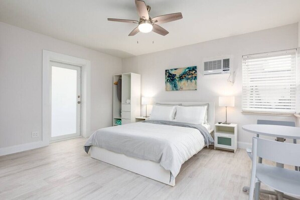 A bedroom with a bed, a ceiling fan, a bedside table, a chair, and a window with blinds.