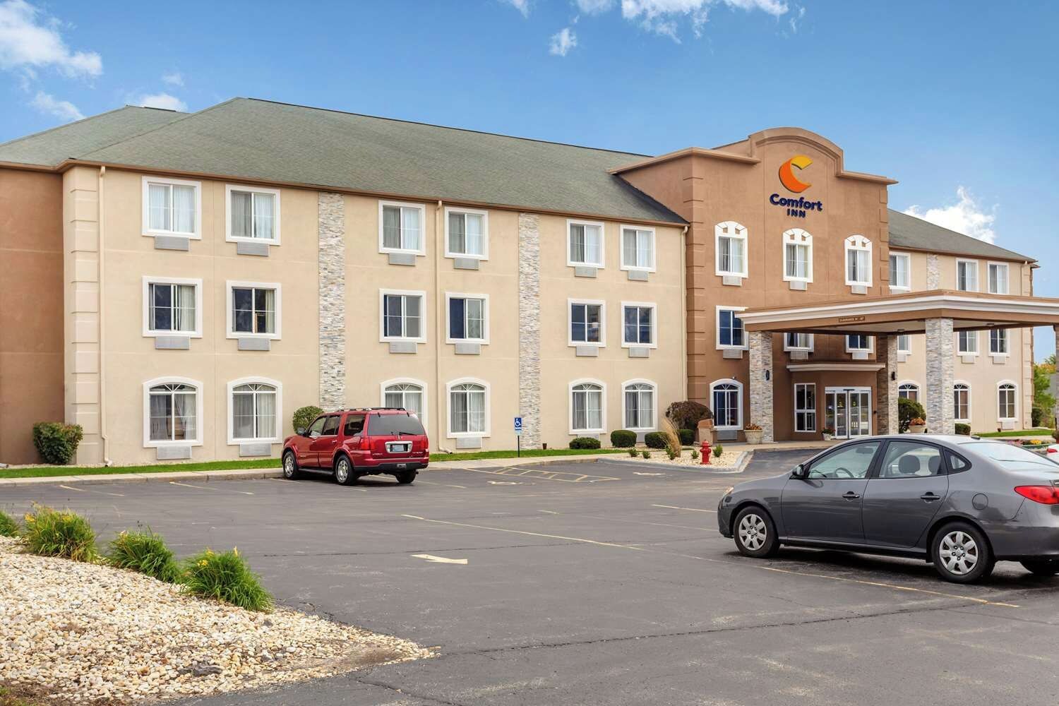 A hotel with a central entrance, multiple windows, and a parking lot with cars.