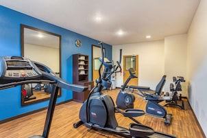 A gym with cardio machines, a mirrored wall, and a wooden floor.