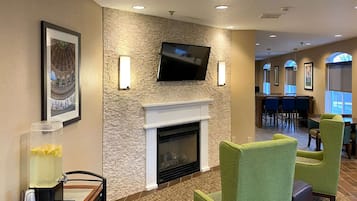 A hotel lobby with a fireplace, a television mounted on a stone wall, and a bar area in the background.
