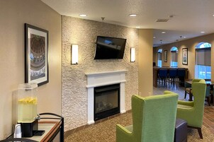 Un hall de hotel con chimenea, televisión montada en una pared de piedra y una zona de bar al fondo.