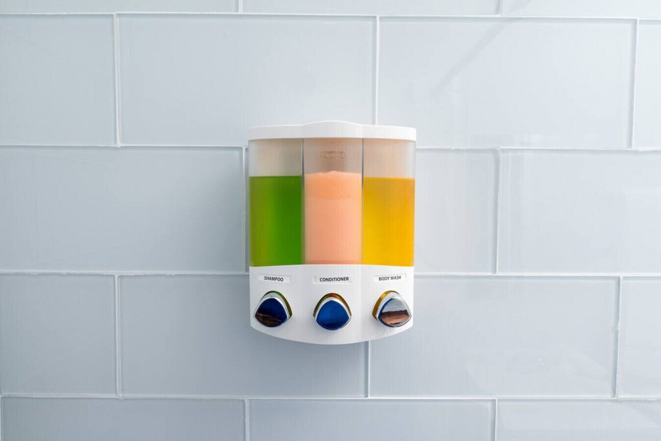 A wall-mounted dispenser with three compartments containing different colored liquids, labeled for shampoo, conditioner, and body wash.