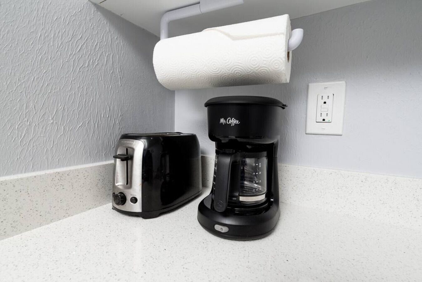 A kitchen area with a toaster and a Mr. Coffee coffee maker on a countertop.