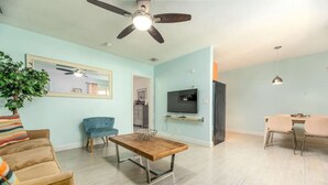 A living room with a ceiling fan, a TV mounted on the wall, a dining table with chairs, and a sofa. - Steps to Sand & Sea #3 (Lauderdale-by-the-Sea)