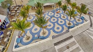 A beachfront hotel with a central courtyard featuring palm trees and a patterned floor, a pier extending into the ocean, and a beach area with umbrellas and beach chairs. - Steps to Sand & Sea #3 (Lauderdale-by-the-Sea)