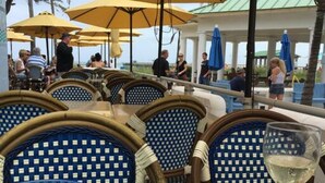 Un espace extérieur aménagé pour les repas, avec des chaises en osier et des parasols jaunes, donnant sur une piscine.