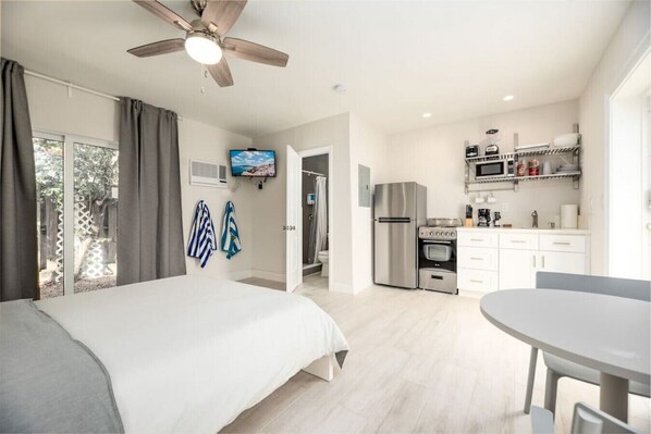 Una habitación de hotel moderna con una cama, una mesa de comedor, una kitchenette y un ventilador de techo.
