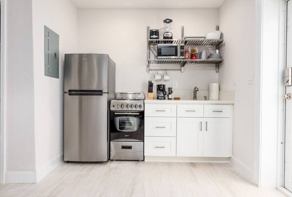 Cocina compacta con refrigerador de acero inoxidable, horno empotrado, microondas y cafetera sobre la encimera.