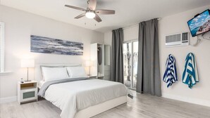 A modern bedroom with a bed, bedside tables, a ceiling fan, a large window with curtains, and a wall-mounted TV. - Ocean Flats #3 - Lauderdale-by-the-Sea (Lauderdale-by-the-Sea)