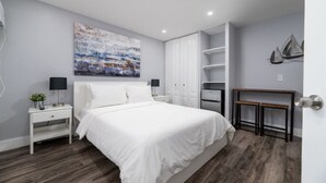 A modern bedroom with a large bed, white nightstands, a desk, and a wardrobe. - Shell on the Beach #103 (Hollywood)