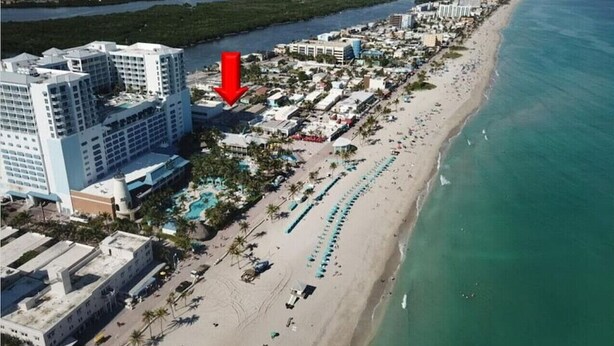 An aerial view of a coastal hotel with multiple buildings, a beach, and a marina. - Shell on the Beach #103 (Hollywood)