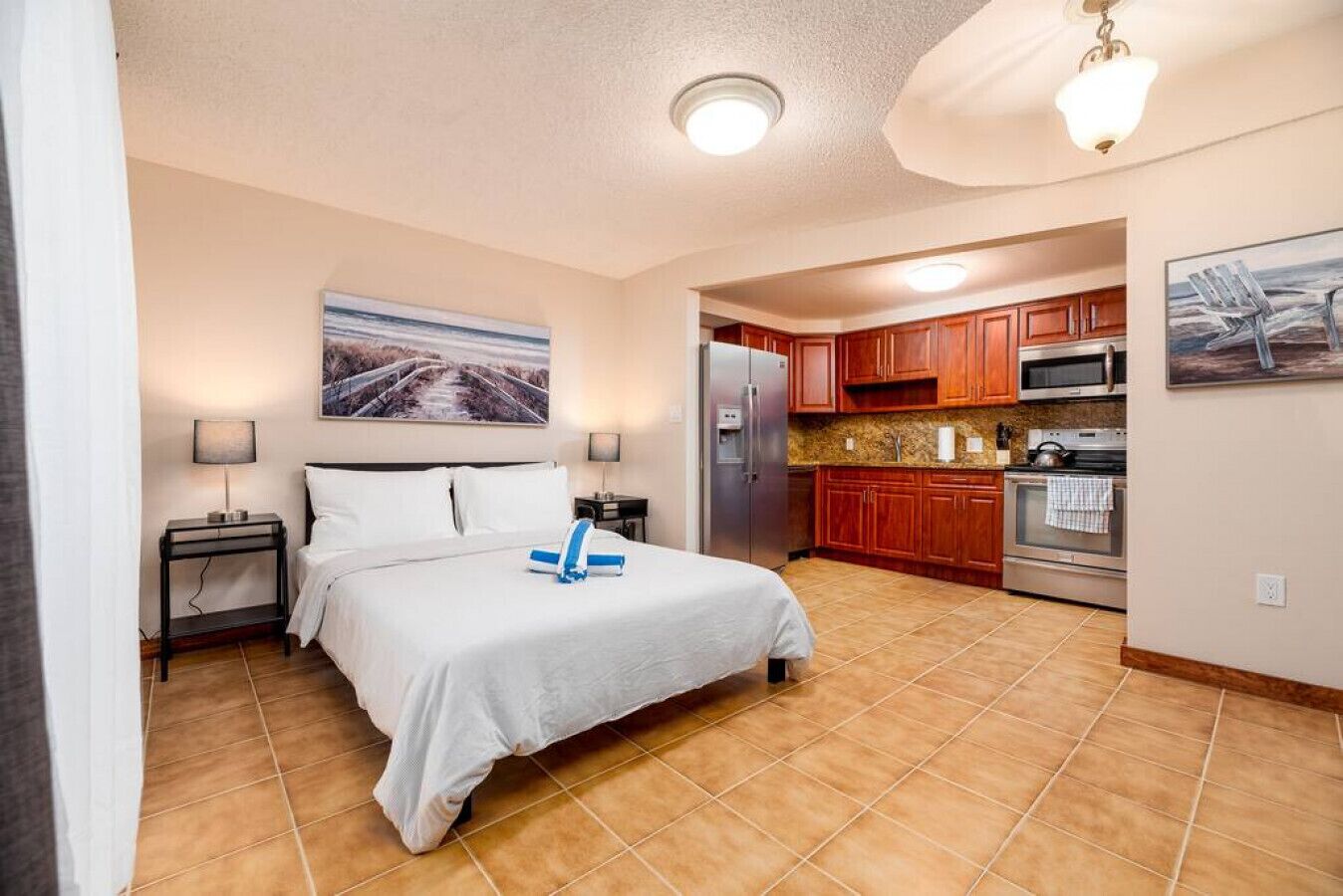 A hotel room with a bed, a nightstand, a lamp, a refrigerator, a microwave, and a kitchen area with cabinets and a countertop.